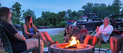 A group of people sitting around a stone fire pit in an outdoor setting.