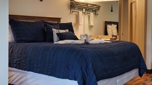 A neatly made bed with a dark blue quilt and white linens, a wooden headboard, a wall-mounted light fixture, and a mirror with a towel rack. - Timber Pointe Resort (Jamestown)