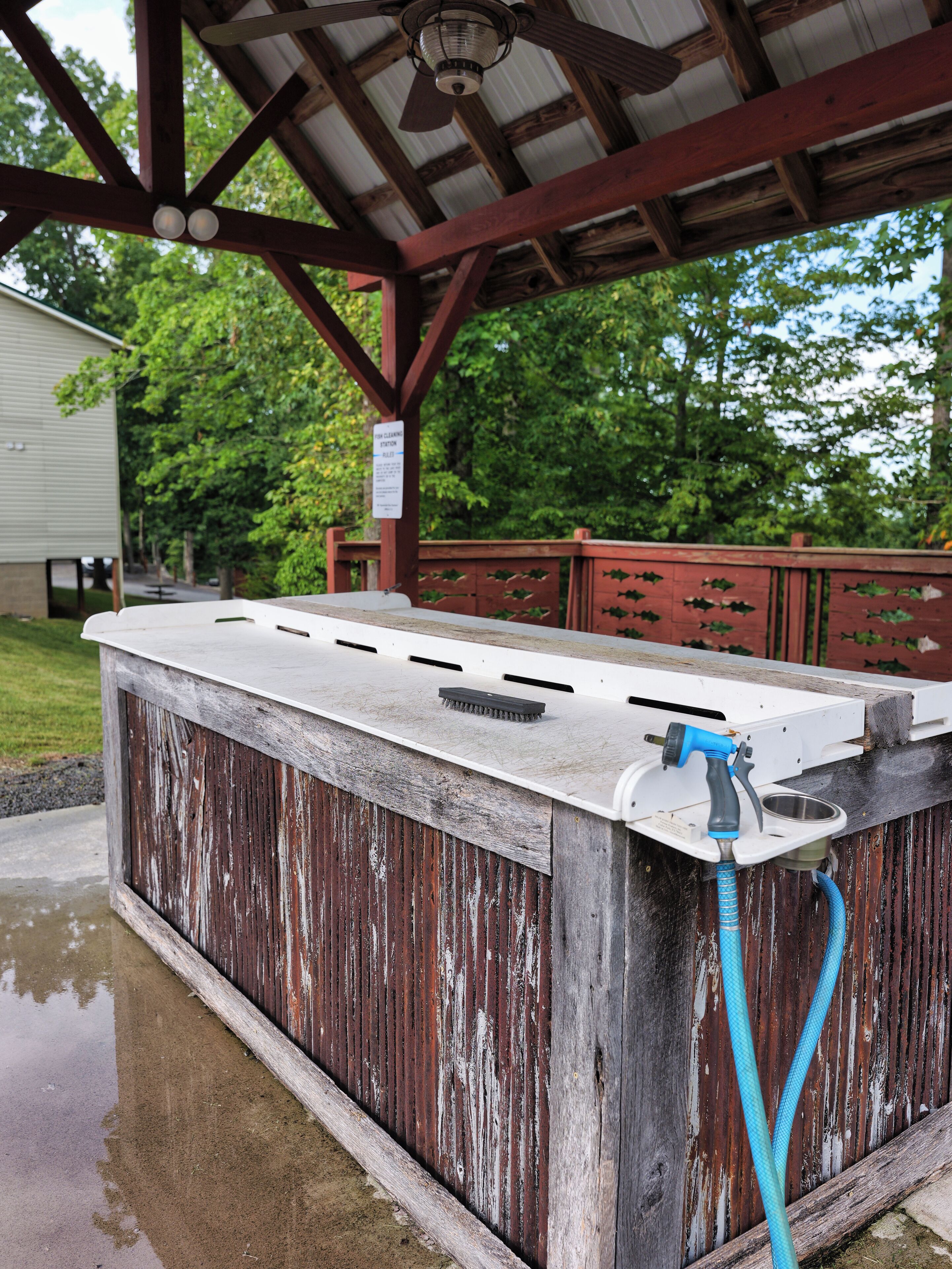 A rustic outdoor bar with a wooden structure, a metal roof, and a hose attached to the side.