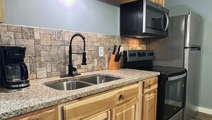 A kitchen with wooden cabinets, a granite countertop, a stainless steel sink, a coffee maker, a microwave, a refrigerator, and an oven. - Timber Pointe Resort (Jamestown)