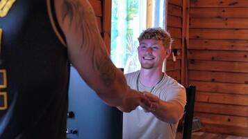A wooden interior with a person wearing a white shirt and a black sleeveless top with a visible number.