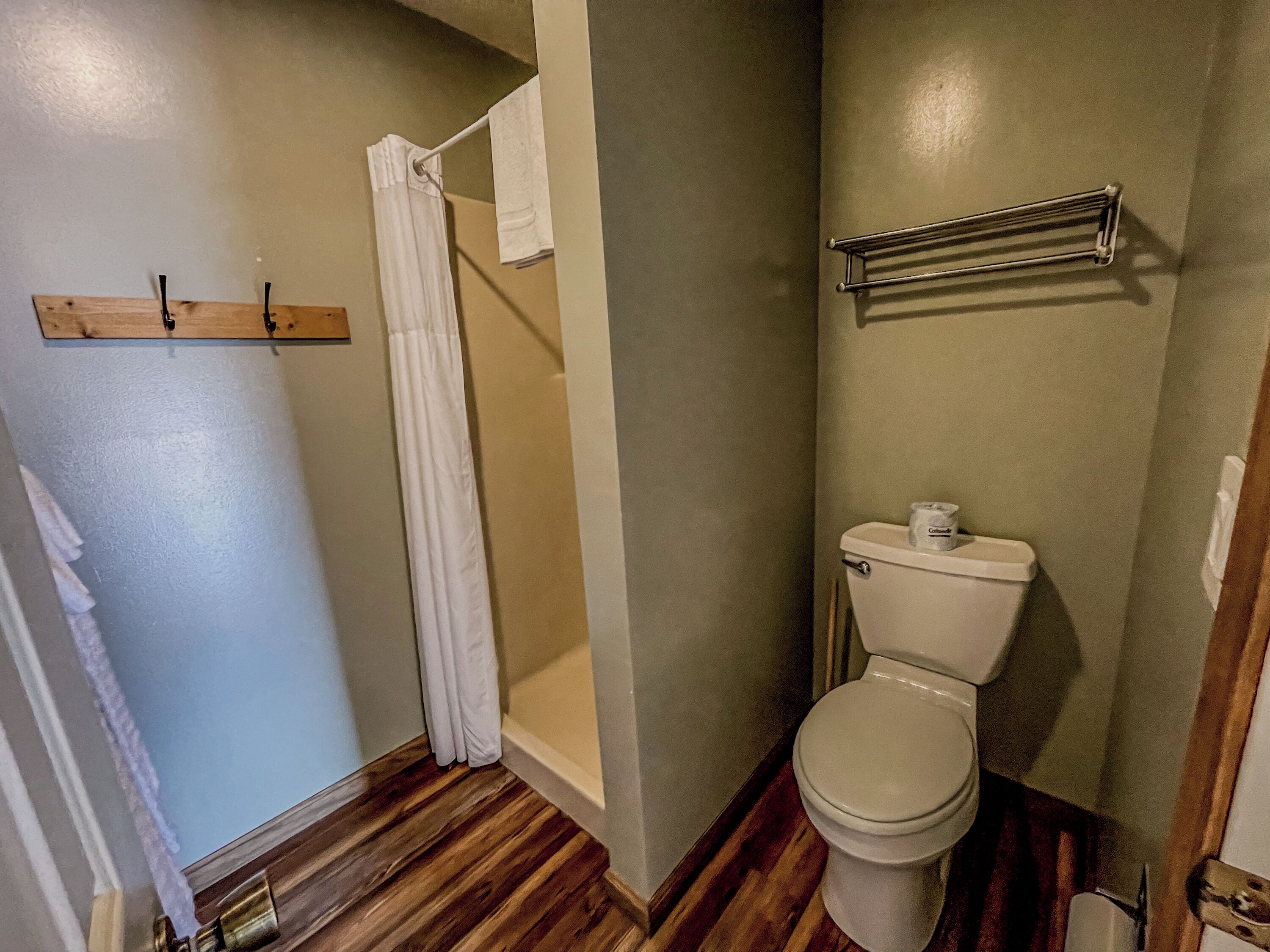 Un bagno con pavimento in legno, un water bianco, una tenda da doccia e un porta asciugamani.