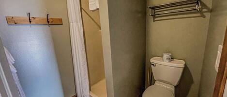 A bathroom with a wooden floor, a white toilet, a shower curtain, and a towel rack.