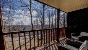 A covered outdoor area with a wooden deck, wicker furniture, and a view of a forested landscape. - Timber Pointe Resort (Jamestown)