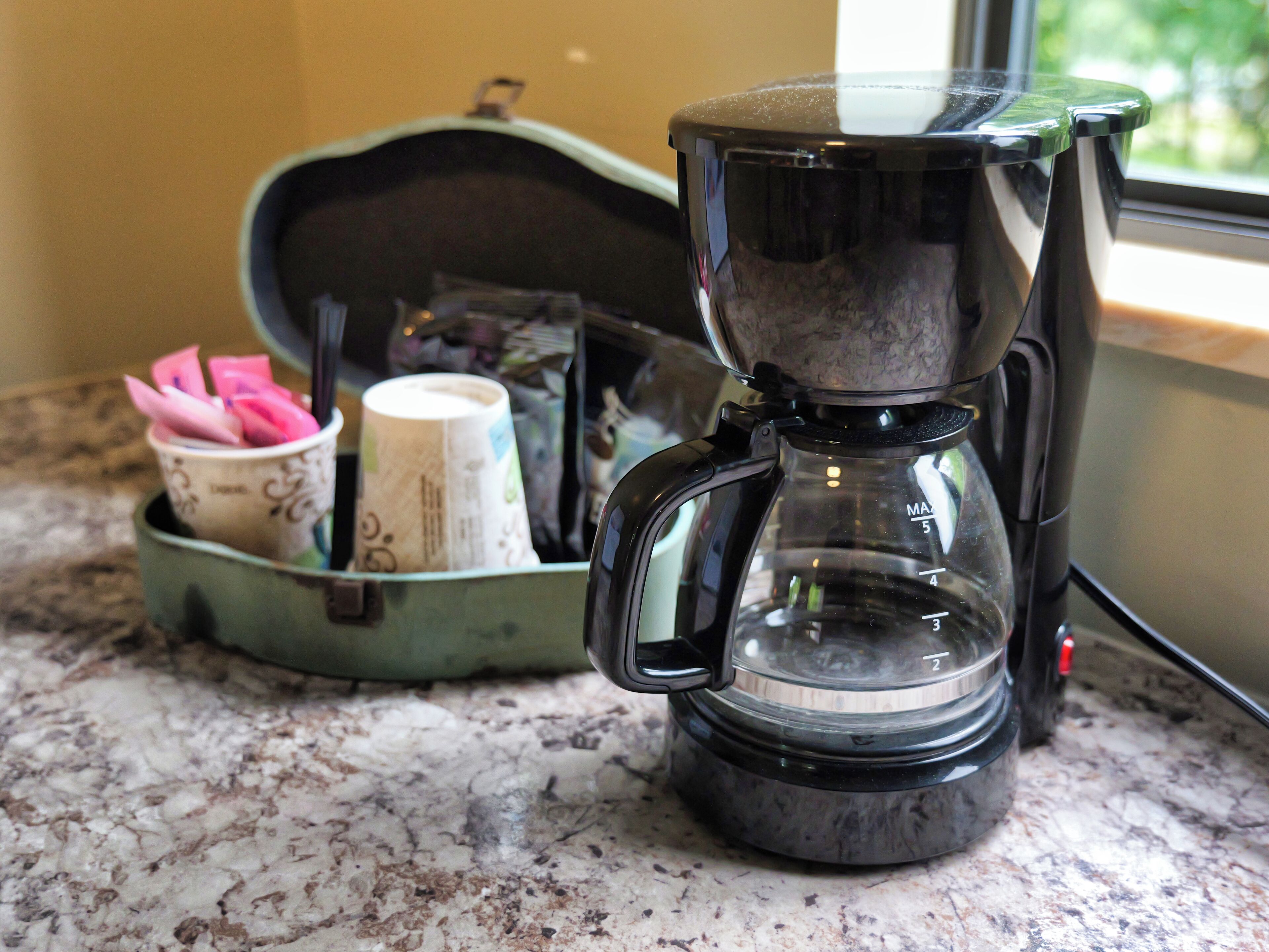 A coffee maker on a kitchen counter with a cup of coffee and a cup of tea.