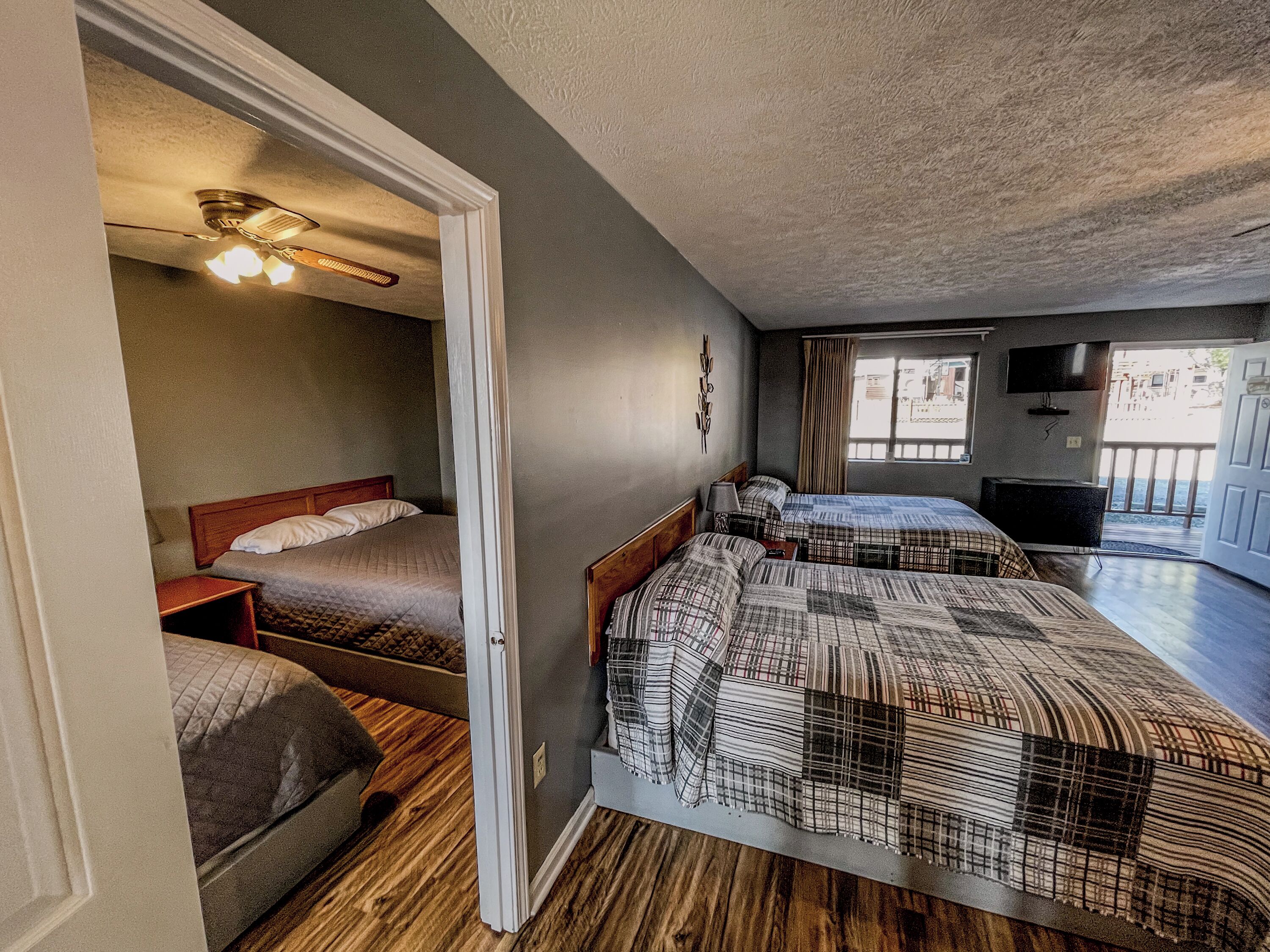 A room with two beds, a ceiling fan, a TV, and a window with curtains.