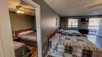 A room with two beds, a ceiling fan, a TV, and a window with curtains.