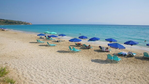 Una playa con hileras de sombrillas azules y verdes, y sillas reclinables.