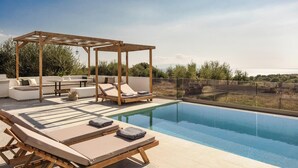 Zona de piscina en la azotea con sillones de descanso, una pérgola de madera y vista al mar.