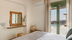 Un dormitorio con cama, espejo, aire acondicionado de pared, una mesita con un jarrón y vistas a una piscina y al paisaje a través de una puerta de cristal.