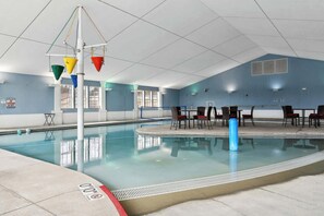 Ein Hallenbad mit Rettungsschwimmerstuhl, einem Tisch mit Stühlen und einer blauen Wand.
