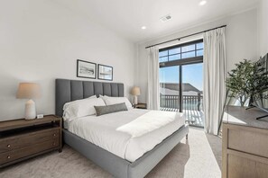 Ein modernes Schlafzimmer mit einem großen Bett, zwei Nachttischen mit Lampen, Blick auf einen Balkon und einer Topfpflanze.