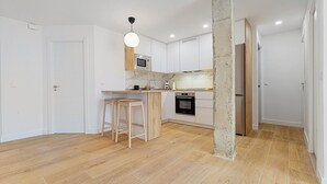 Una cocina moderna con armarios blancos, encimera de madera, microondas, horno y un taburete de bar.