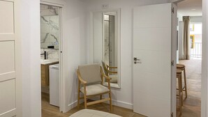 Habitación de hotel con una silla de madera, una cama, un baño con pared de azulejos de mármol y vistas al balcón.
