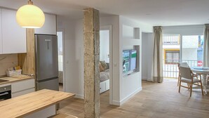 Una cocina moderna con refrigerador empotrado, un comedor con mesa y sillas de madera, y una sala de estar con televisor montado en la pared.