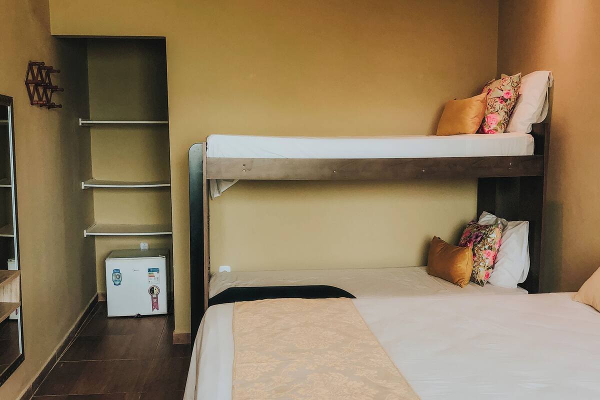 Une chambre d’hôtel avec un lit superposé, un petit réfrigérateur et une étagère.