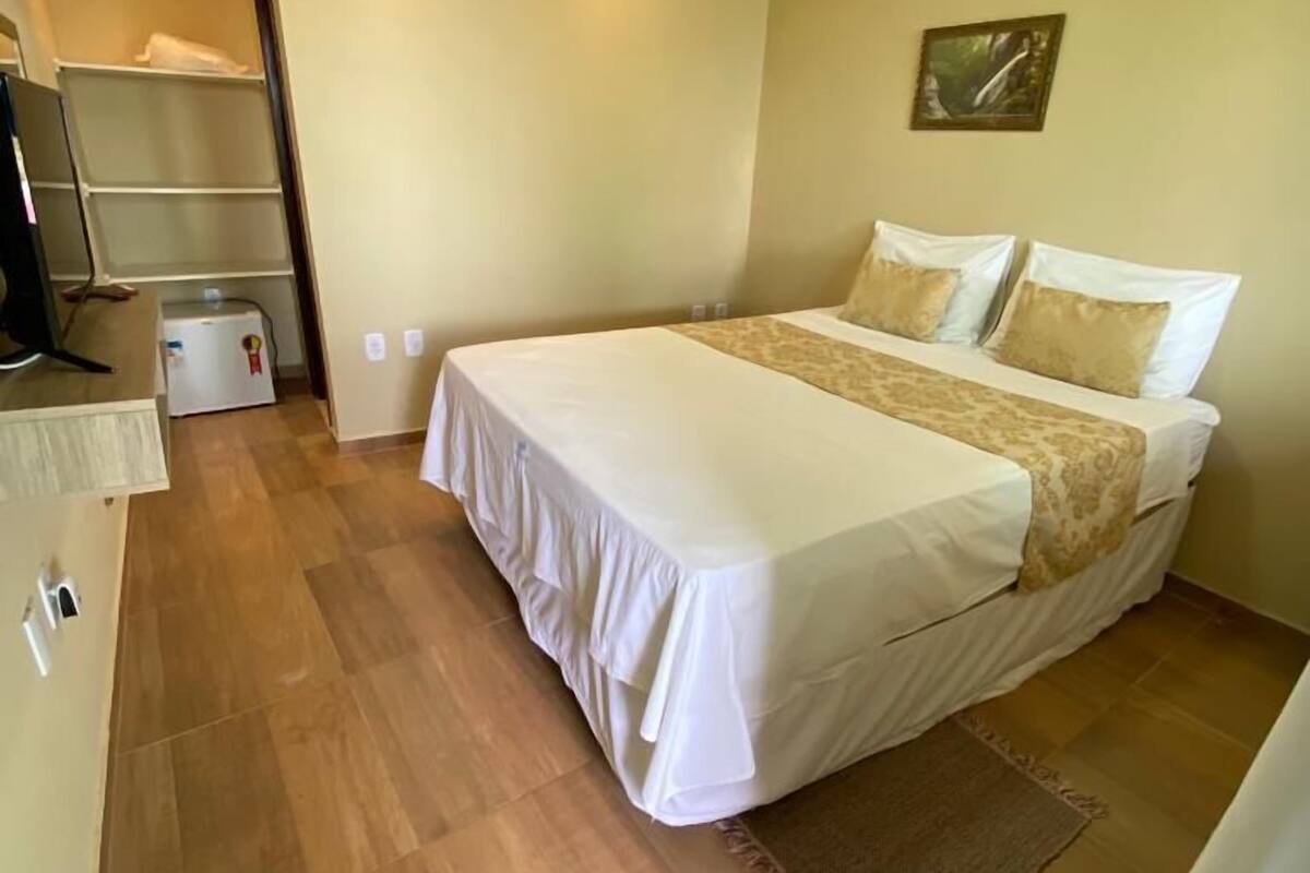 Une chambre d’hôtel avec un grand lit, un bureau, une chaise, une télévision et un petit réfrigérateur.