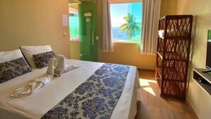 Une chambre d’hôtel avec un lit, une télévision, une fenêtre avec des rideaux et une vue sur l’océan.