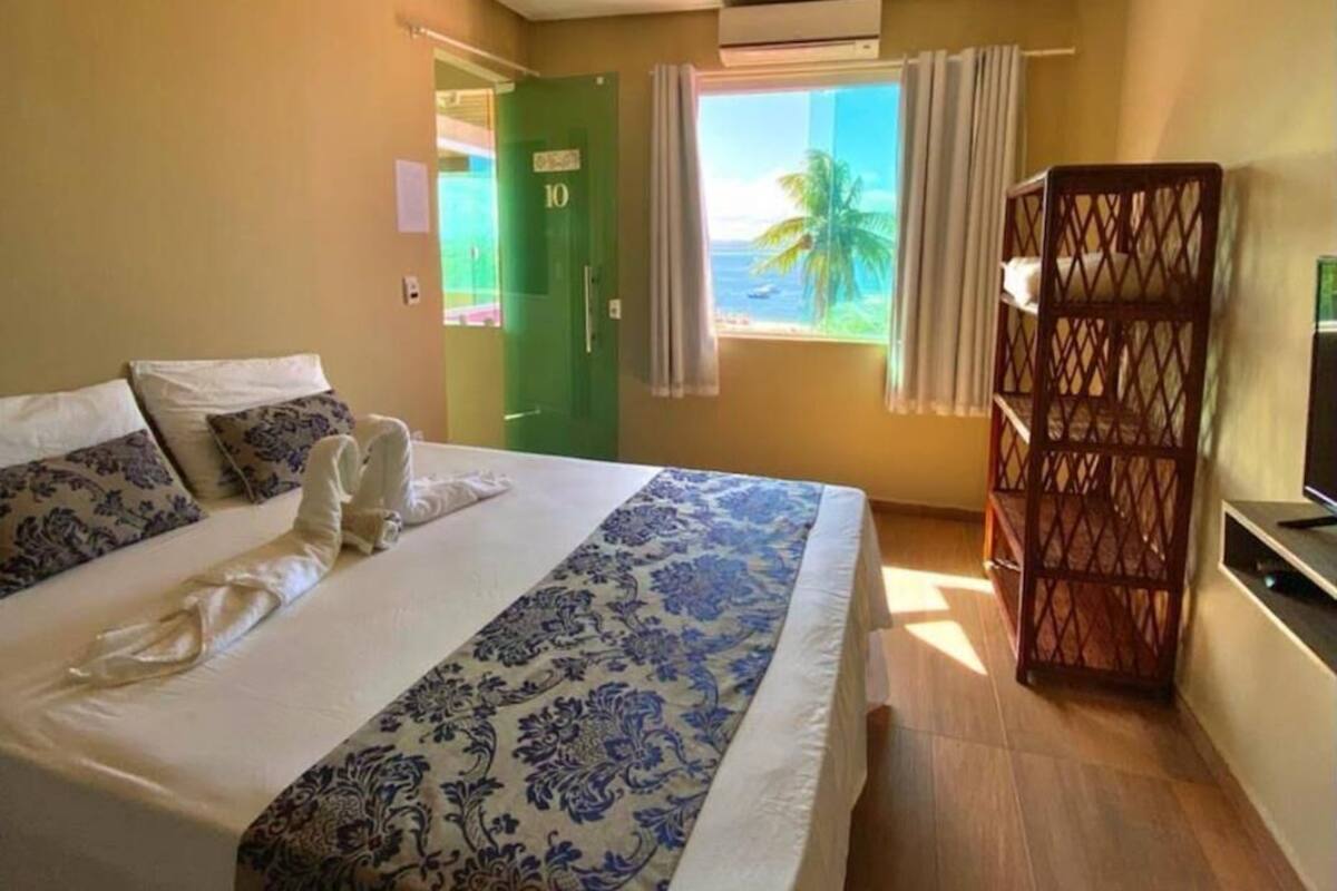 Une chambre d’hôtel avec un lit, une télévision, une fenêtre avec des rideaux et une vue sur l’océan.