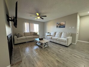 A living room with two sofas, a coffee table, a ceiling fan, and a painting on the wall.
