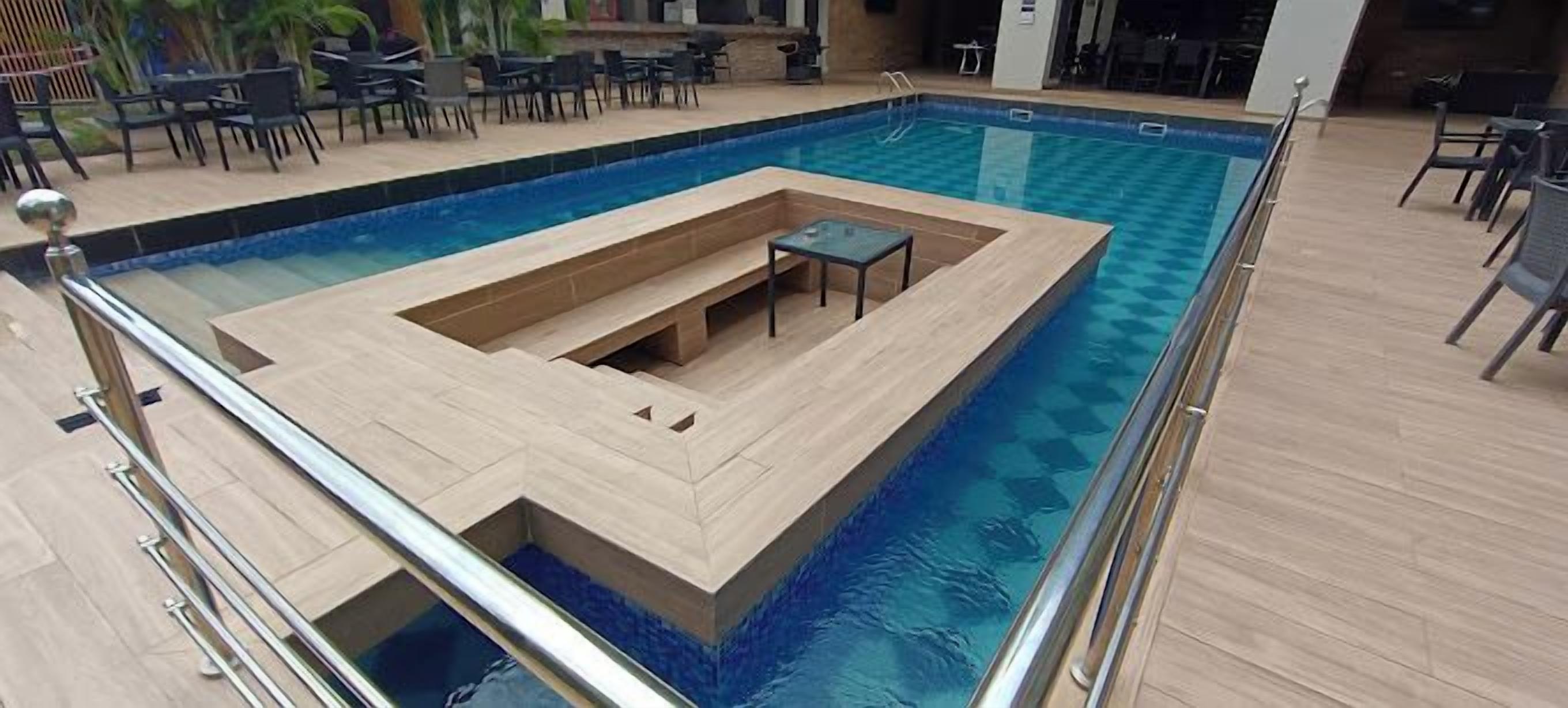 A swimming pool with a sunken seating area, surrounded by a poolside deck and outdoor furniture.