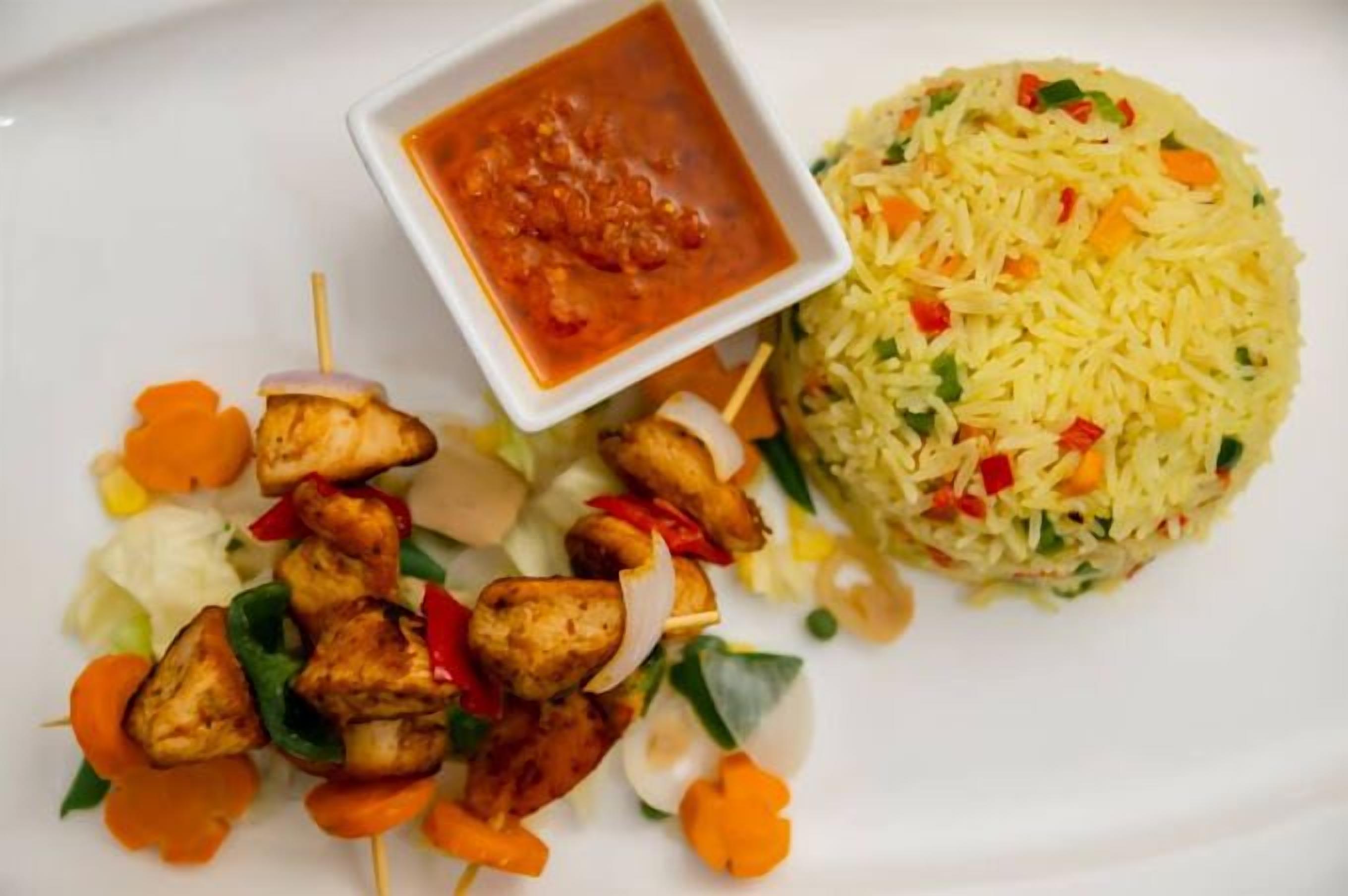 Un plato con brochetas de pollo a la parrilla, una ensalada y una porción de arroz mezclado con vegetales.