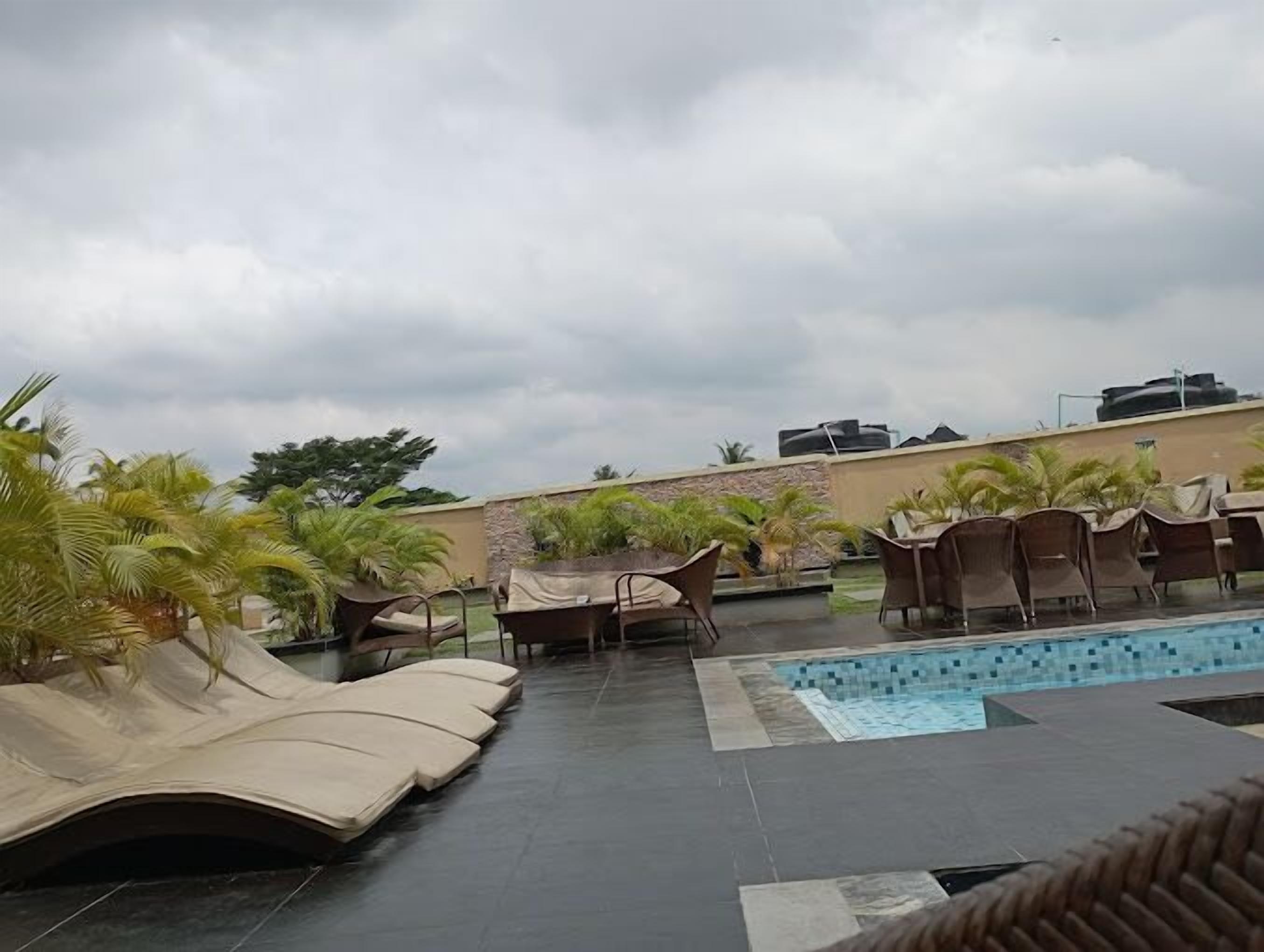 Un área de piscina en la azotea con sillas de descanso y palmeras.