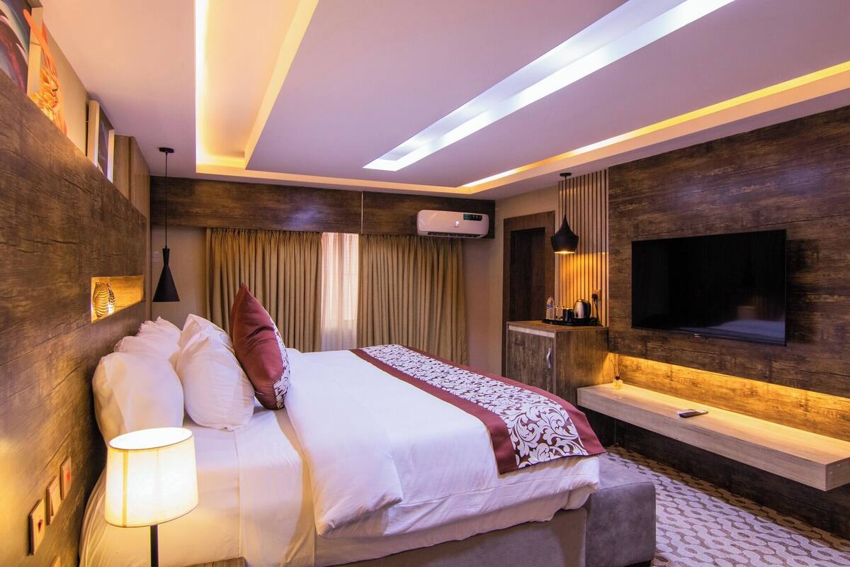 Une chambre d’hôtel moderne avec un grand lit, un téléviseur fixé au mur, une table de chevet et un luminaire au plafond.