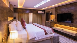 Una habitación de hotel moderna con una cama grande, un televisor montado en la pared, una mesita de noche y una lámpara en el techo.