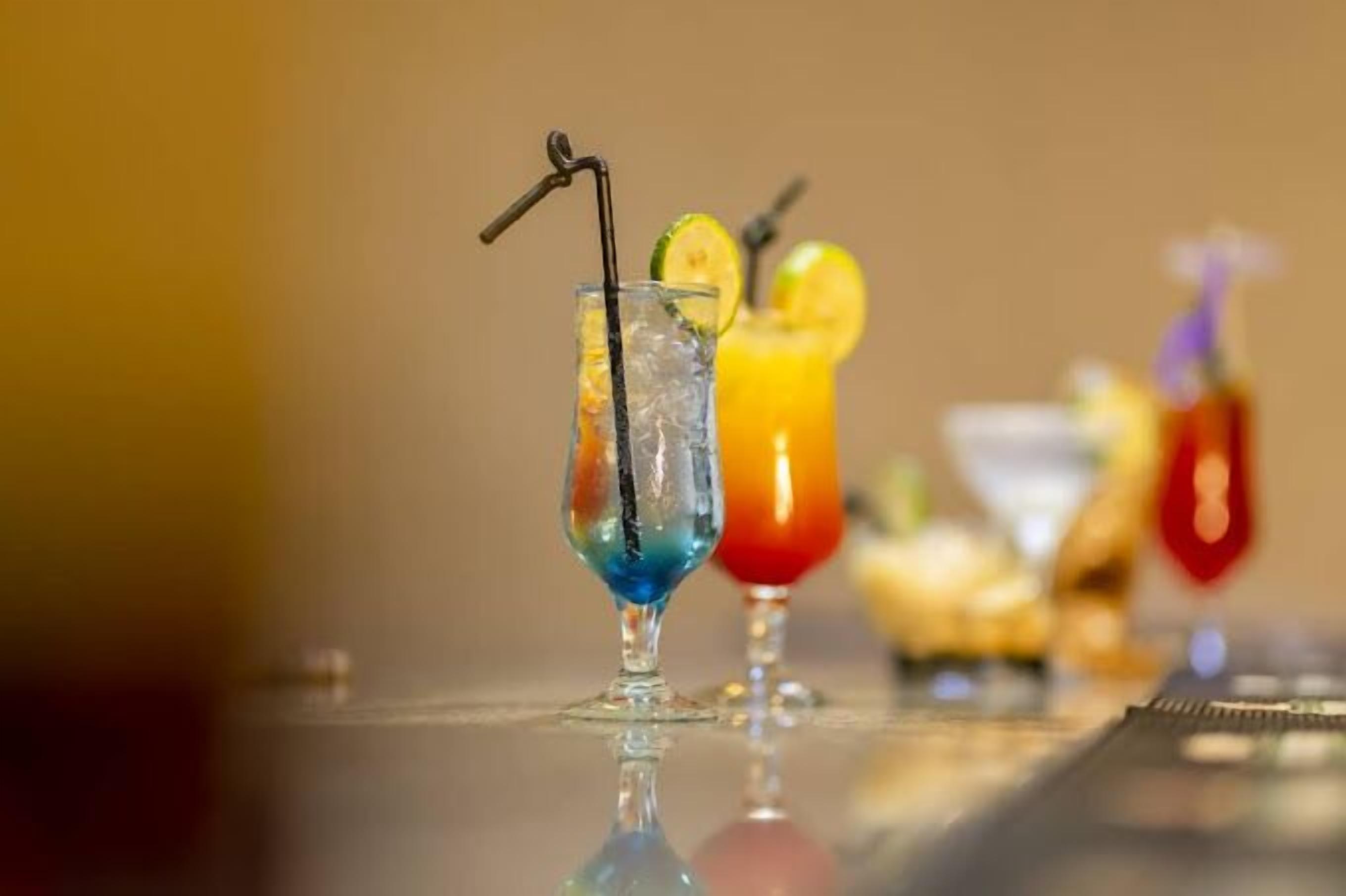 Two cocktails with straws and lime slices on a reflective surface.