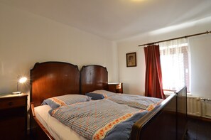 A bedroom with a wooden bed, a nightstand, a lamp, a window with curtains, and a radiator. - Holiday Home for 8 People in Butgenbach (Buetgenbach)