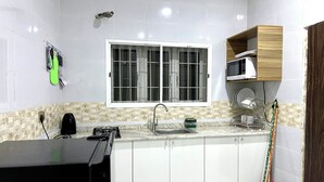 Eine moderne Küche mit weißen Schränken, einer schwarzen Arbeitsplatte, einem Fenster mit Metallgitter und einem Besen, der an der Wand lehnt.