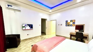 Habitación de hotel con cama, escritorio, silla, televisor e iluminación azul en el techo.