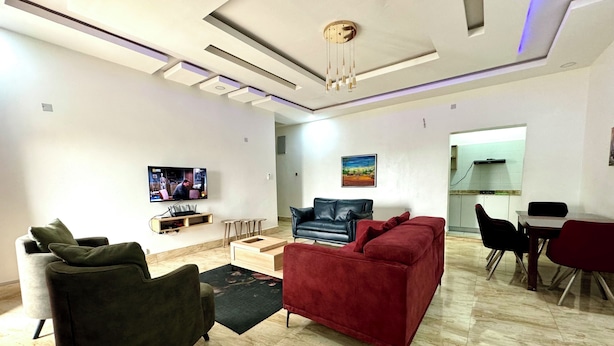 Una sala de estar moderna con un televisor de pantalla plana, un sofá rojo, un sofá de cuero negro y un comedor con mesa y sillas.
