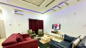 Una sala de estar moderna con un sofá rojo, sillones verdes, una mesa de centro de madera y un sofá negro. Hay un televisor de pantalla plana montado en la pared.