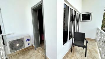 A balcony with a chair, a window, and a door leading to a room.