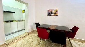 Un comedor con una mesa de madera y sillas rojas, una cocina con armarios blancos y un cuadro en la pared.