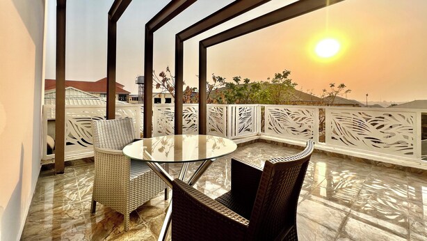 A balcony with a glass table and wicker chairs, overlooking a residential area during sunset. - SUNSET VIEW PENTHOUSE CONDO at UTAKO ABUJA. 24hrs LIT with AC, WIFI & KITCHEN (Abuja)