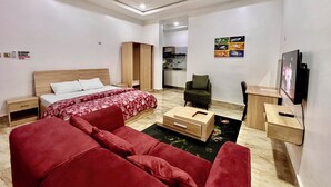 A modern hotel room with a bed, red upholstered sofa, wooden wardrobe, and a TV. - SUNSET VIEW PENTHOUSE CONDO at UTAKO ABUJA. 24hrs LIT with AC, WIFI & KITCHEN (Abuja)