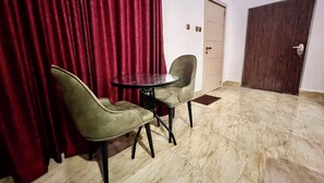 A room with a red curtain, a round table, two chairs, a door, and an air conditioning unit on the wall. - SUNSET VIEW PENTHOUSE CONDO at UTAKO ABUJA. 24hrs LIT with AC, WIFI & KITCHEN (Abuja)