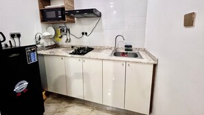 A compact kitchen with white cabinets, a microwave, a gas stove, and a sink. - SUNSET VIEW PENTHOUSE CONDO at UTAKO ABUJA. 24hrs LIT with AC, WIFI & KITCHEN (Abuja)