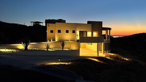A modern house with a flat roof, large windows, and a well-lit driveway. - Desert Retreat: Heated Salt Water Plunge Pool* Grill, Views, Cinema,nearBalandra (La Paz)