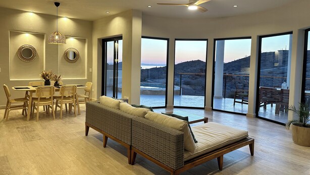 A spacious living room with a large sofa, dining area, and a view of a mountainous landscape through large windows. - Desert Retreat: Heated Salt Water Plunge Pool* Grill, Views, Cinema,nearBalandra (La Paz)