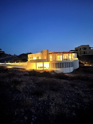 Una casa moderna de dos pisos con techo plano, ventanas amplias y un patio cubierto.