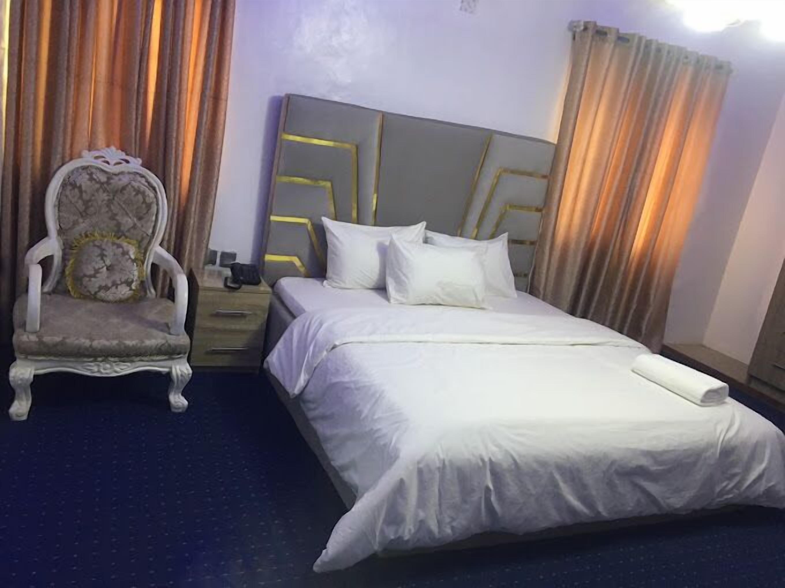 A hotel room with a large bed, a nightstand, a chair, and curtains.