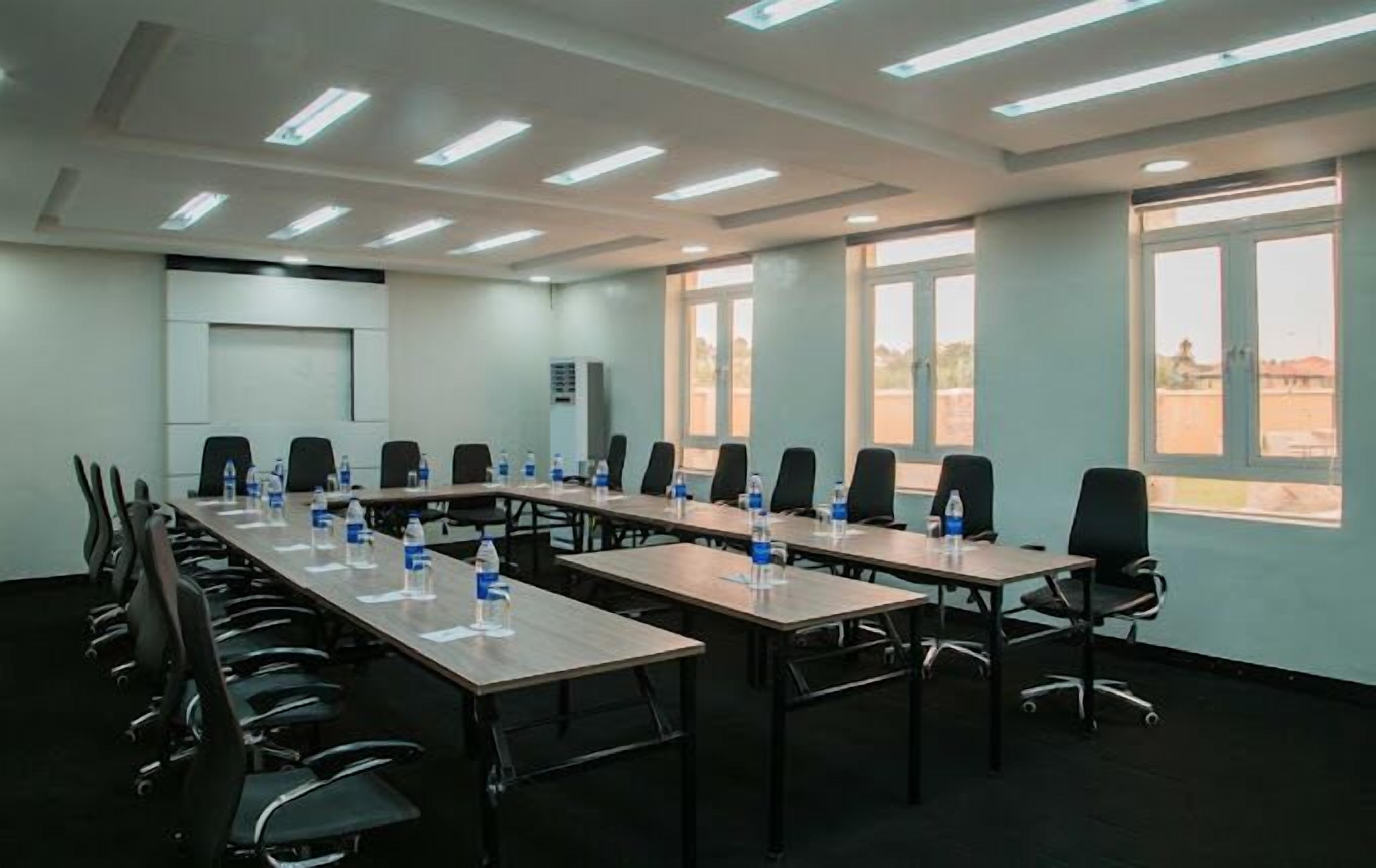 Un salón de conferencias con largas mesas, sillas y botellas de agua.