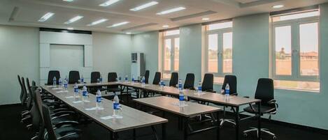 Un salón de conferencias con largas mesas, sillas y botellas de agua.