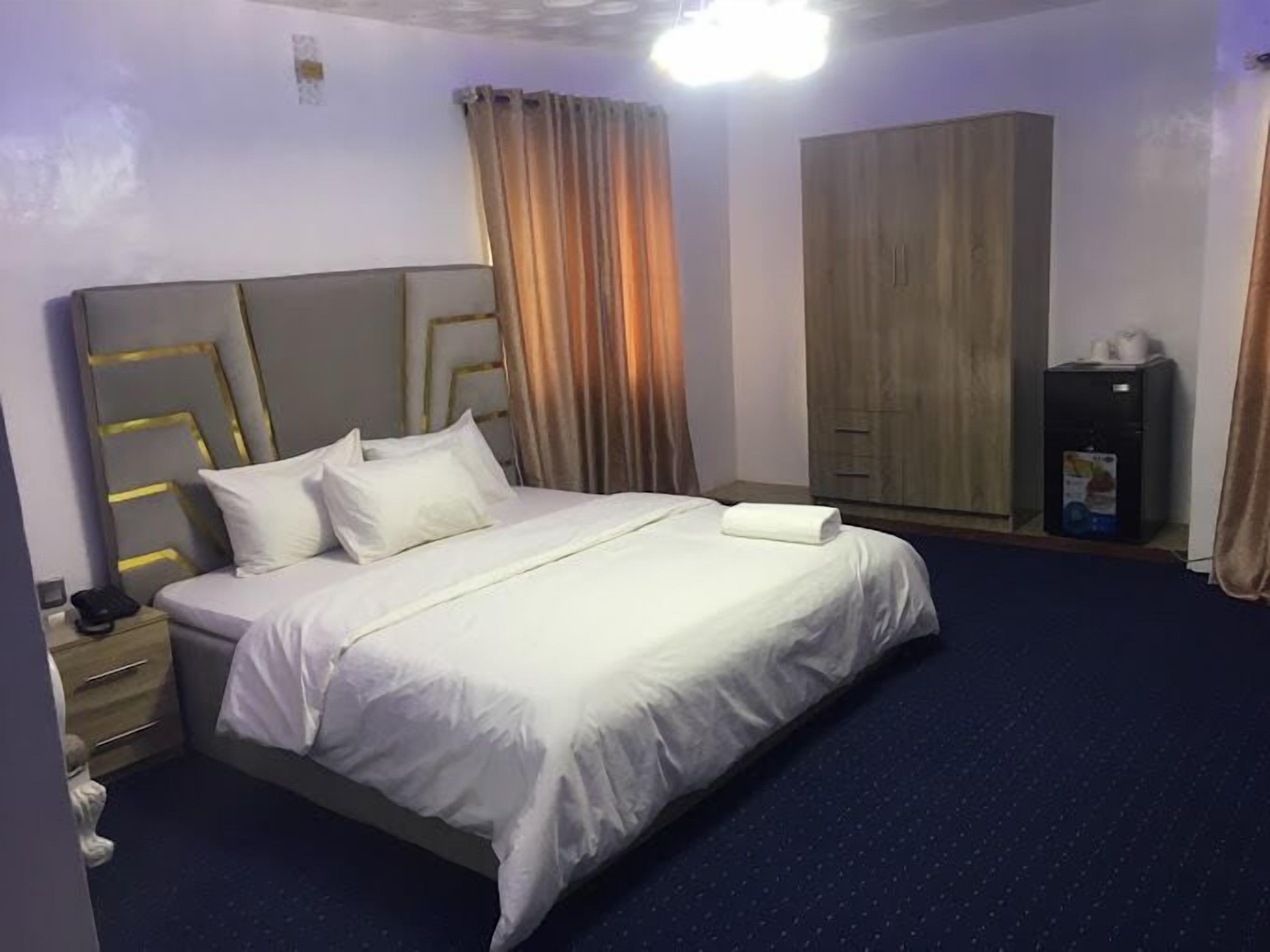 Una habitación de hotel con cama, armario, escritorio con lámpara y minibar.
