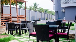 An outdoor seating area with wicker tables and chairs, a patterned floor, and a low wall with a fence. - Dee Rocket Hotel (Ibadan)