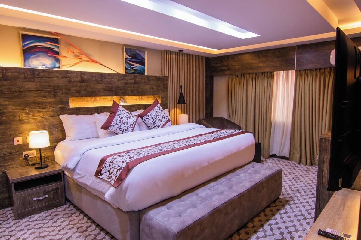 Habitación de hotel elegante con una cama grande, una mesita de noche con lámpara, una televisión y una obra de arte colgada en la pared.